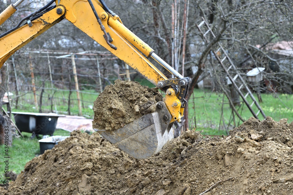 Fototapeta premium A road excavator digs soil on the foundations of an outbuilding to the house