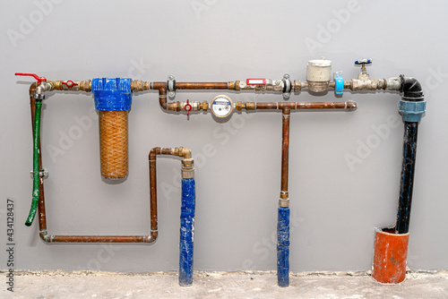 Two pipes with cold water flowing from the floor and a valve from the main water supply, domestic plumbing, visible copper pipes and a meter. photo