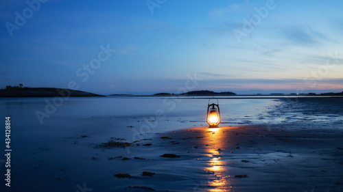 Fototapeta Naklejka Na Ścianę i Meble -  Vintage oil lamp on the sea at sunset. Oantern burning with an orange soft flame. Blurred background.

