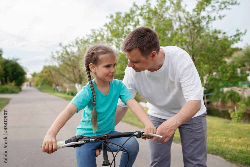 Father teaching her little daughter to ride a bicycle, happy summer in village, healthy lifestyle, childhood, fatherhood and upbringing, concept for father day Father teaching her little daughter to ride a bicycle, happy summer in village, healthy lifestyle, childhood, fatherhood and upbringing, concept for father day