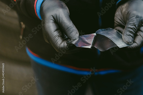 Pair of gloved hands peeling duct tape from a small piece of leather for steering wheel