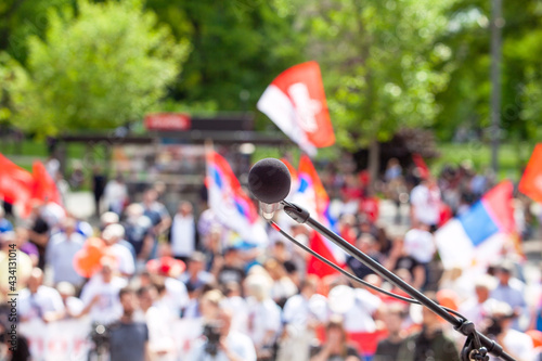 Political protest or public demonstration, focus on microphone, blurred crowd of people holding flags in the background