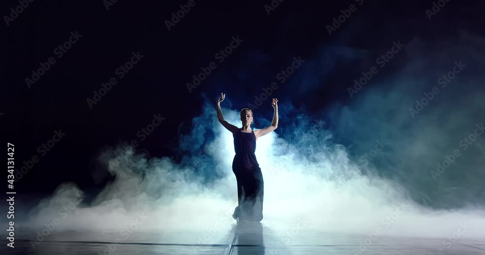 A young attractive girl in a black elegant dress is slowly dancing. She squats a little, raises her arms up. Then she very smoothly spreads them in different directions and rotates them A young attractive girl in a black elegant dress is slowly dancing. She squats a little, raises her arms up. Then she very smoothly spreads them in different directions and rotates them