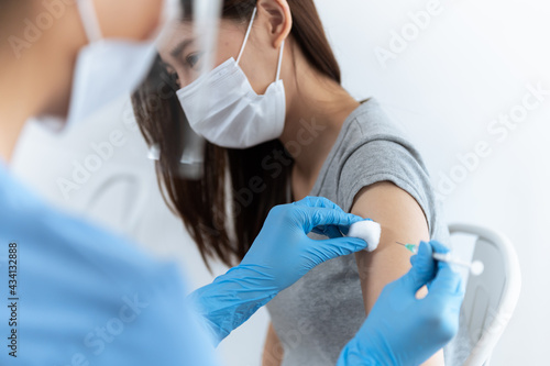 Asian woman nurse injecting covid-19 vaccine to young Thai woman patient wearing mask in clinic or health care center. Coronavirus pandemic protection or health care medical concept.