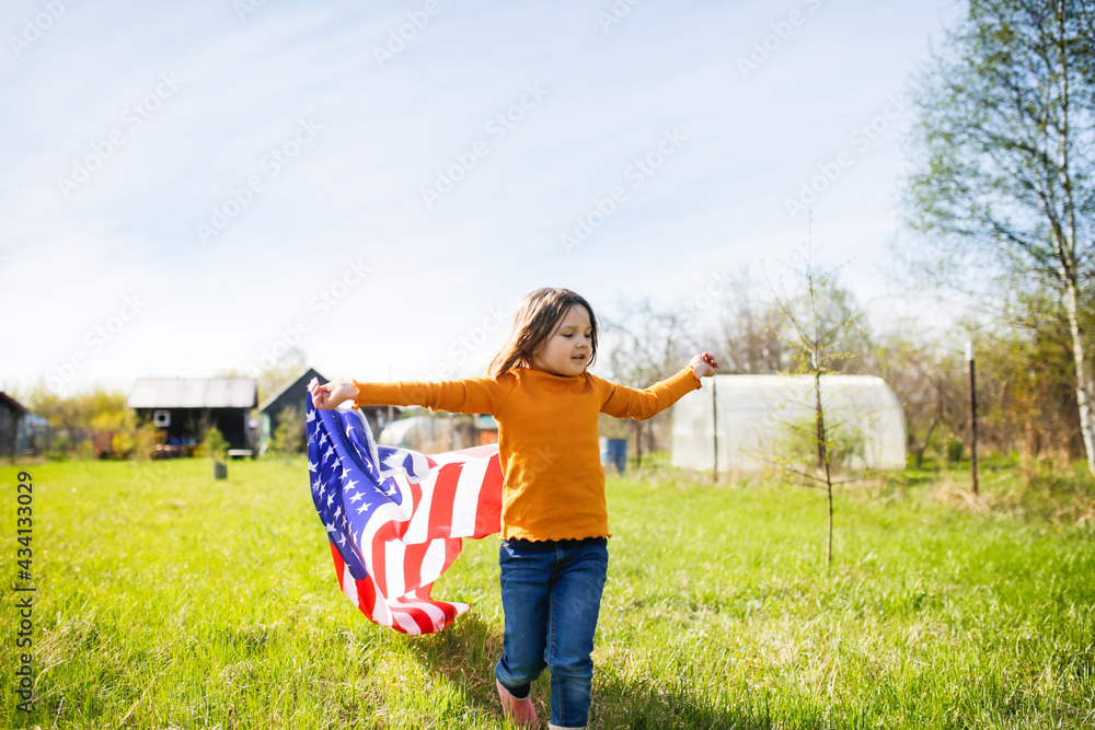 Happy American kid girl with waving USA flag on independence day. Child running with the USA flag at a picnic on July 4th