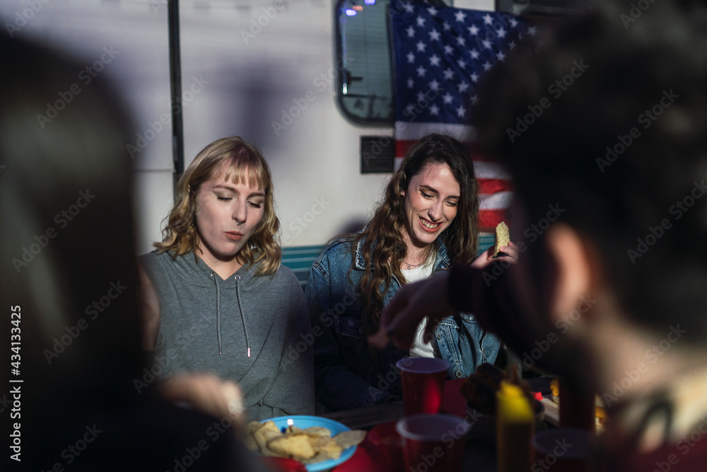 Grupo de amigos comiendo barbacoa por el día de la independencia de estados unidos de américa junto a una caravana con la bandera americana