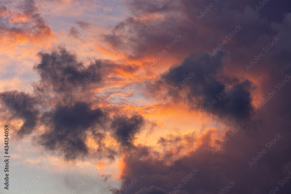 Dark patches of clouds in shadow with radiant vibrant colorful red, yellow and orange sunset colors. Weather conditions and climate concept. Abstract background wallpaper poster.