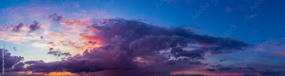 Wide panorama with vibrant blue sky and dramatic sunset contrasting colors of yellow, red and orange touching the cumulus cloud. Weather conditions. Wallpaper poster.