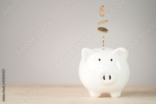 Coins falling and dropping to white piggy bank saving ,money saving for investment and retirement in the future concept.