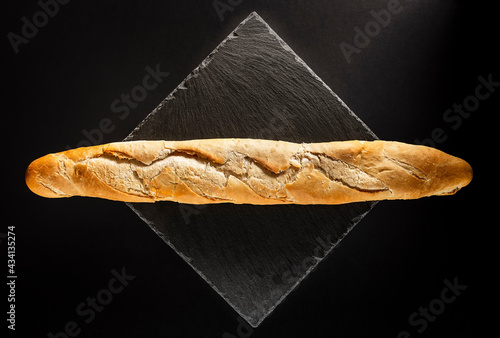 Loaf of artisan bread on a black slate.It is a still life with a black background and a zenithal point of view.The photo is taken in horizontal format. photo