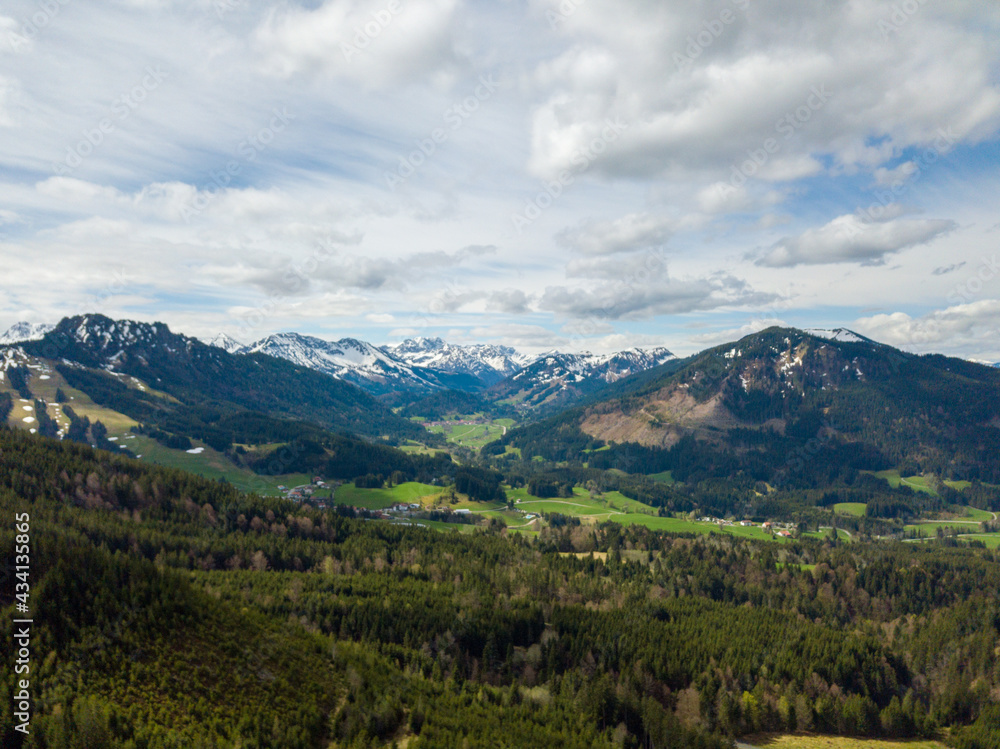 Snowy mountains of the Allgäuer Alpen by aerial - drone view on a party cloudy and sunny day with green trees on the foreground