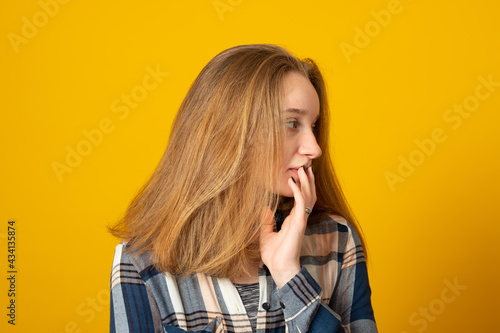 Pleasant looking young girl holds chin and looks pensively away, thinks about great plan, has new ideas in mind, wears checkered shirt.