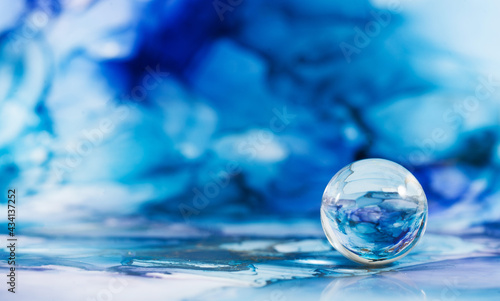 A transparent glass ball on an abstract blue background. The technique of alcoholic ink. Copy space.