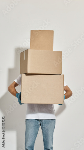 Young redhead deliveryman holding three cardboard boxes standing one on one