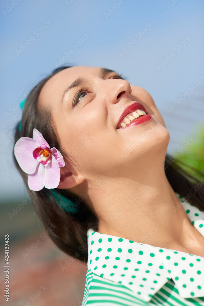 Young woman looking up with hand on forehead and orchid on ear Young woman looking up with hand on forehead and orchid on ear