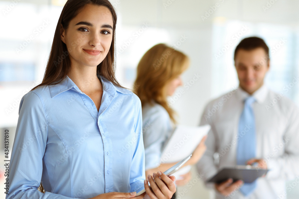 A friendly young dark hair businesswoman or female student is standing with some papers in the office A friendly young dark hair businesswoman or female student is standing with some papers in the office