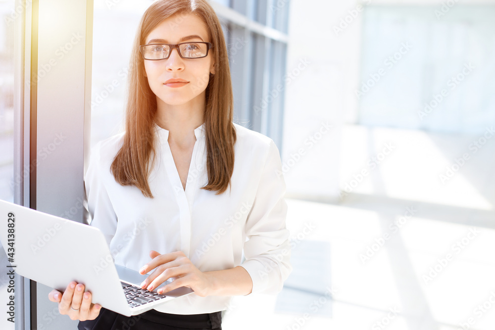 Beautiful female specialist with laptop computer standing in sunny office and smiling charmingly. Business people concept Beautiful female specialist with laptop computer standing in sunny office and smiling charmingly. Business people concept