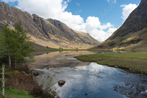 Landscape of Glencoe in Scottish Highlands with reflections in water of loch, mountains including Aonach Eagach ridge to left. Blue sky and clouds. photo