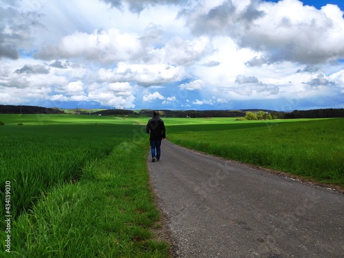 A beautiful Spring scene on a country road in Franconia, Germany as a man goes walking towards a dramatic skyscape.