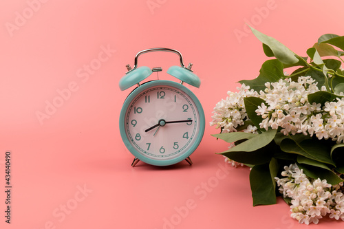 Blue vintage alarm clock with white lilac flowers, isolated on pink background, top view. Perfect morning concept. Deadline and change time concept.