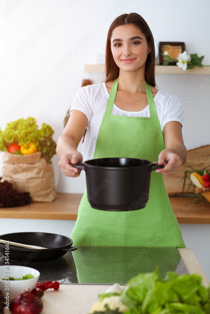 An attractive young dark-haired woman preparing soup by new keto recipe while standing and smiling in sunny kitchen. Cooking and householding concepts An attractive young dark-haired woman preparing soup by new keto recipe while standing and smiling in sunny kitchen. Cooking and householding concepts