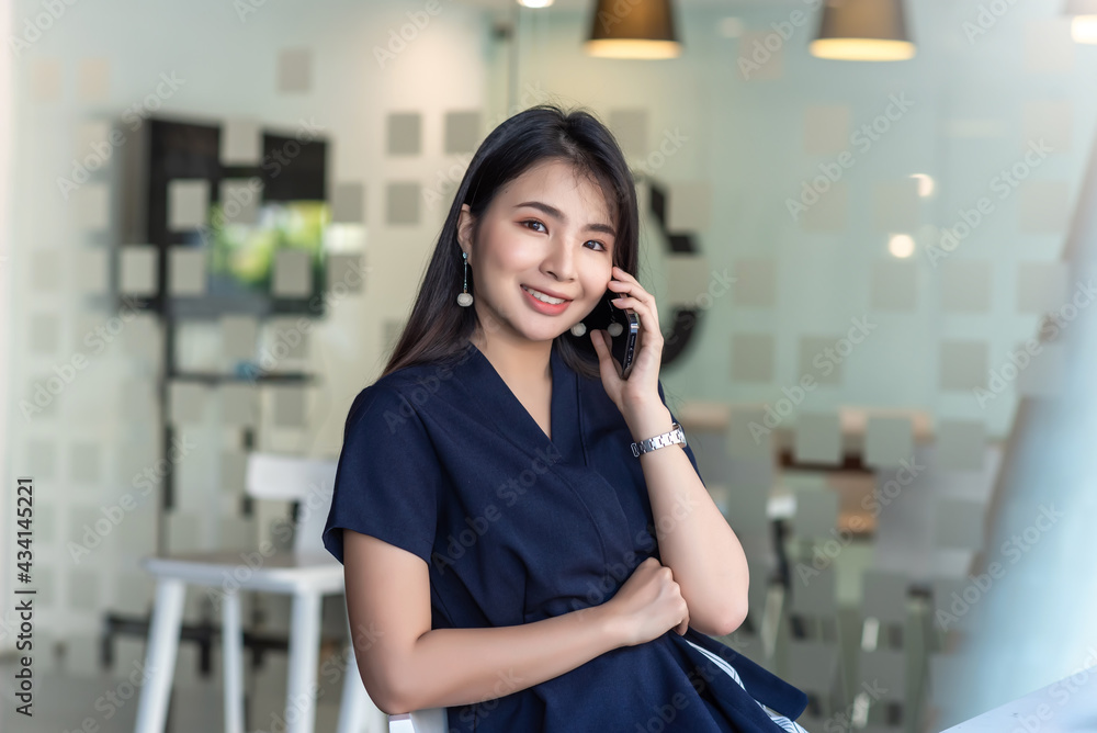Beautiful Asian woman looking at the camera talking on the phone and sitting on a chair. Beautiful Asian woman looking at the camera talking on the phone and sitting on a chair.