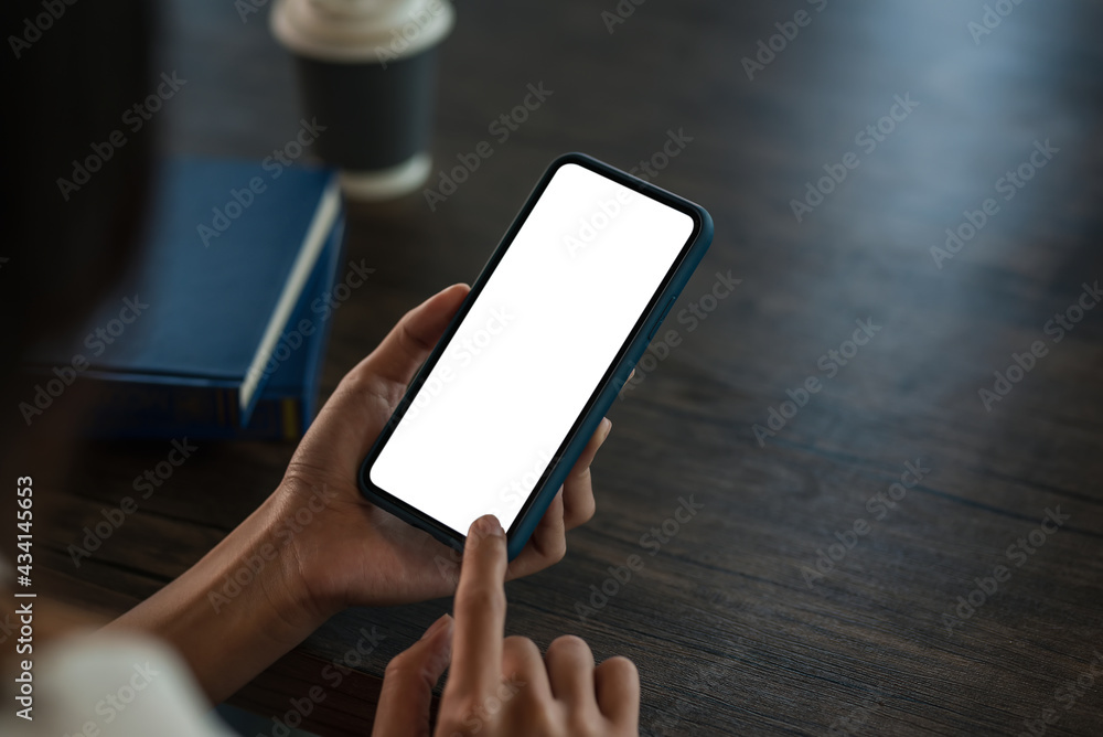 Close up woman hand holding a smartphone blank white screen at office wooden table.
