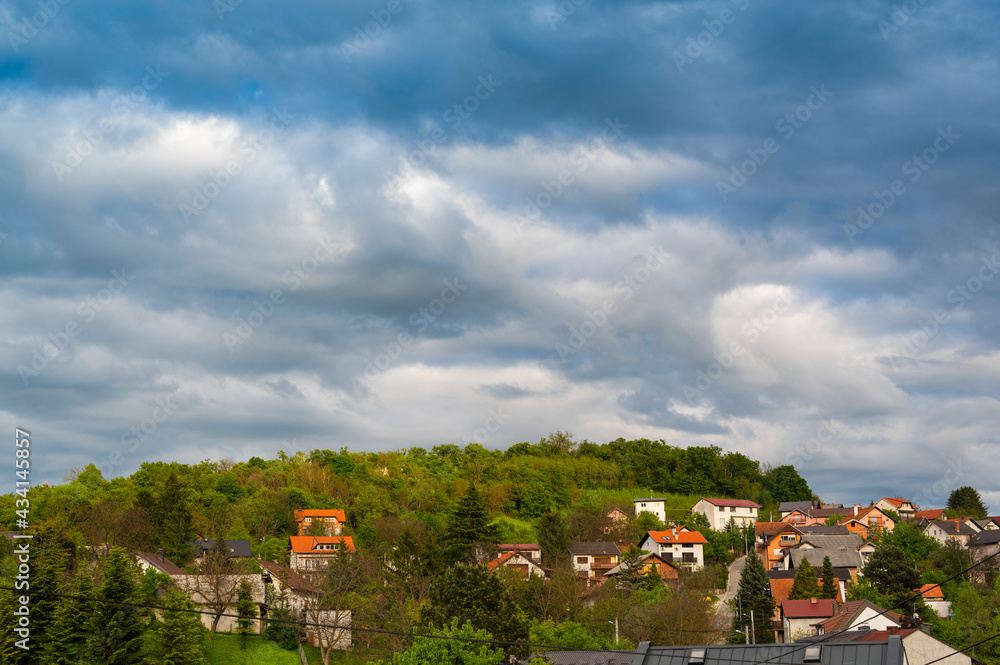 Heavy, rainy clouds over the green hill with houses. Beautiful countryside scenery.