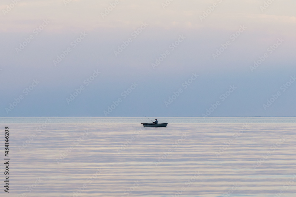 Lonely old fisherman in the rowing boat on the sea. Landscape with a fishing boat in the endless blue calm sea at sunset. Lonely old fisherman in the rowing boat on the sea. Landscape with a fishing boat in the endless blue calm sea at sunset.