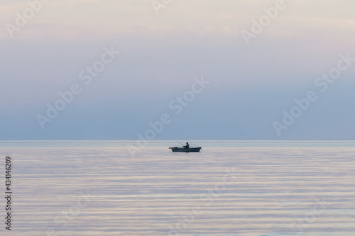 Lonely old fisherman in the rowing boat on the sea. Landscape with a fishing boat in the endless blue calm sea at sunset. © raland