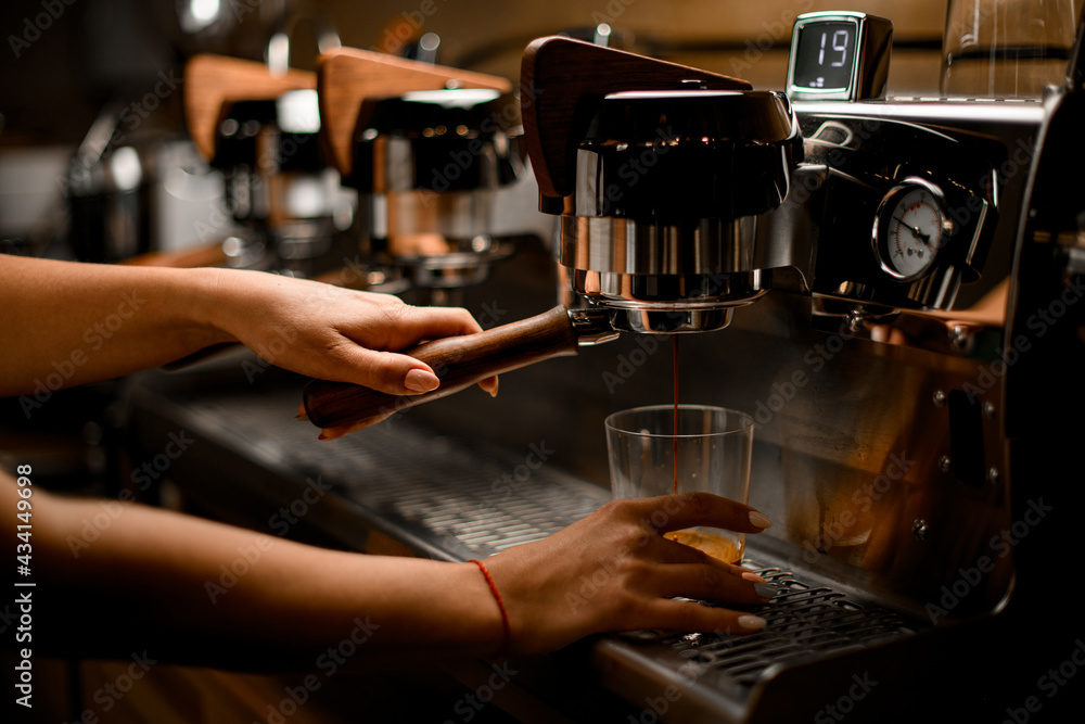 barista's hand controls lever of coffee machine that prepares and pours coffee into glass