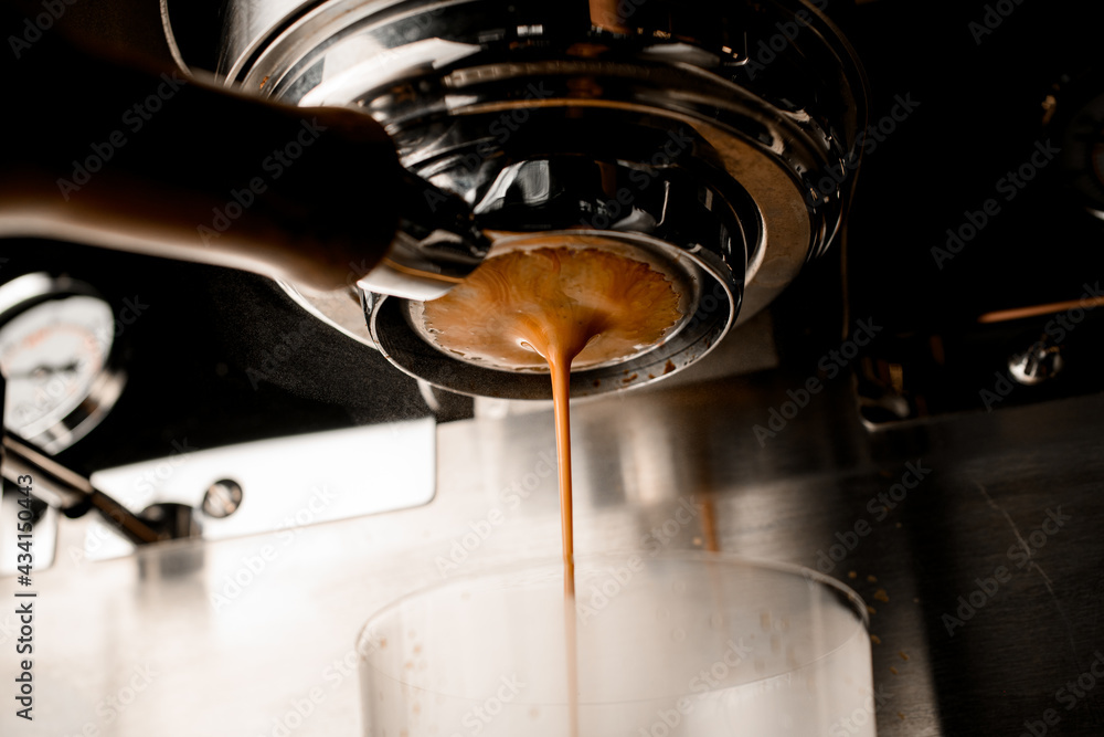 close-up view on portafilter of coffee machine from which espresso flows into glass