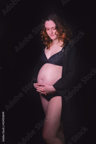 Smiling woman with curly hair holds hands on pregnant belly