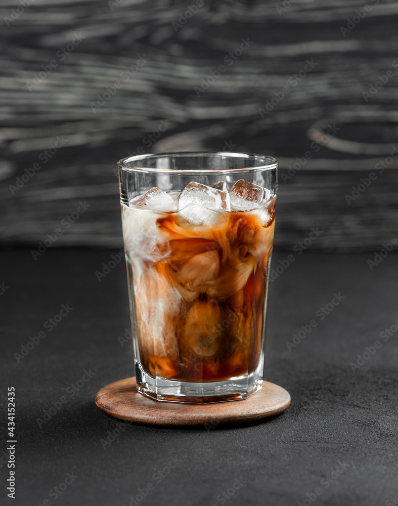 Ice coffee in a tall glass with cream poured. Cold summer drink on a black background with copy space. Ice coffee in a tall glass with cream poured. Cold summer drink on a black background with copy space.