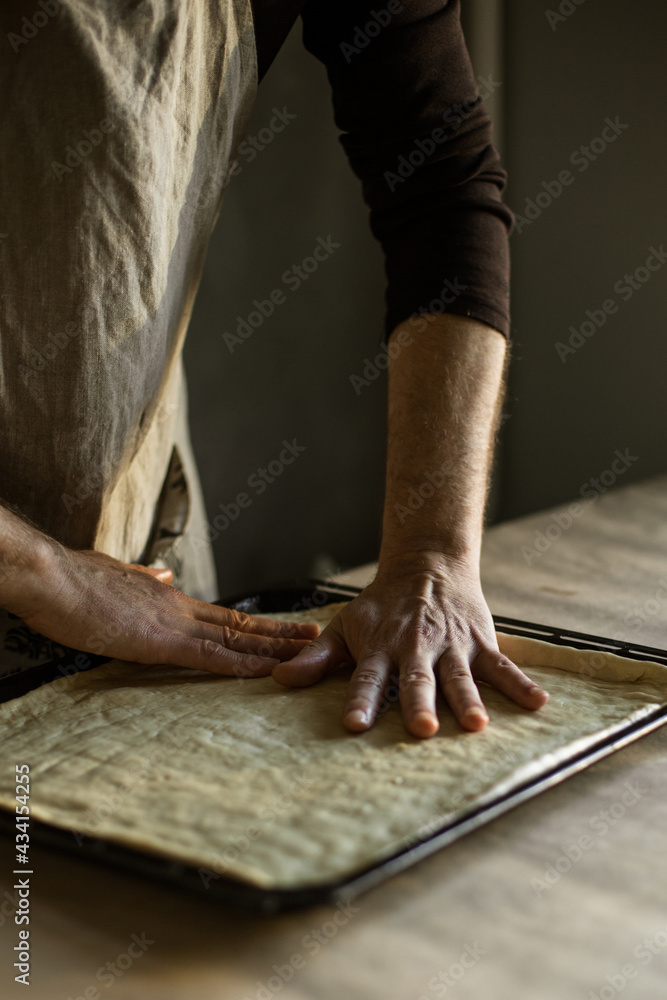 Male hands spreading the dough on a baking sheet Male hands spreading the dough on a baking sheet