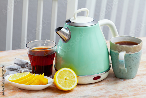 Two cups with fresh black tea on wooden table with vintage light green electric kettle and slices of lemon on plate..