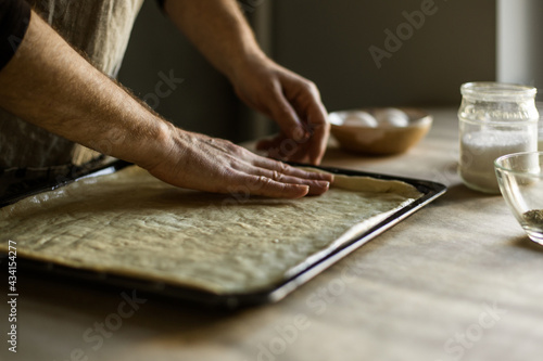 Male hands spreading the dough on a baking sheet