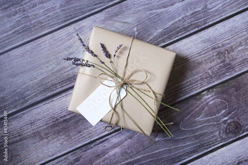 Present wrapped in natural brown paper with lavender flowers and name tag on wooden background. Natural eco friendly packaging. Zero waste gift wrapping idea.