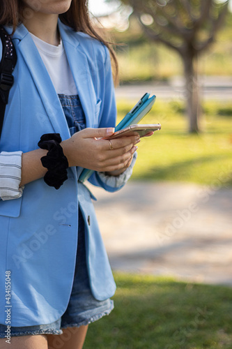 Student girl with glasses uses all kind of technology like laptop, tablet, headphones, telephone and studies at a garden.
