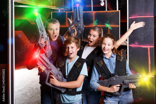 Cheery teens and theirs parents with laser guns during laser tag game indoors