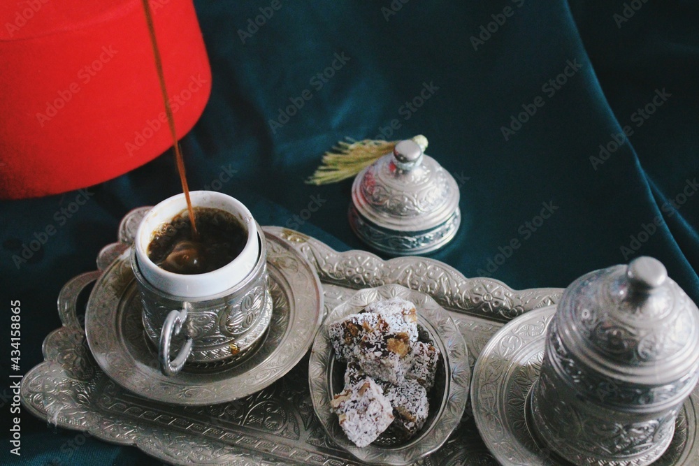 ethnic still life image of traditional ottoman empire fez, turkish coffee pouring to coffee cup and plate with silver arabesque patterns carved & turkish delight  - obrazy, fototapety, plakaty 