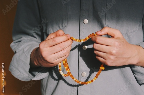 hands of muslim man performing islamic ritual chanting / invocation / dhikr (with both hands) with orange rosary & background photo