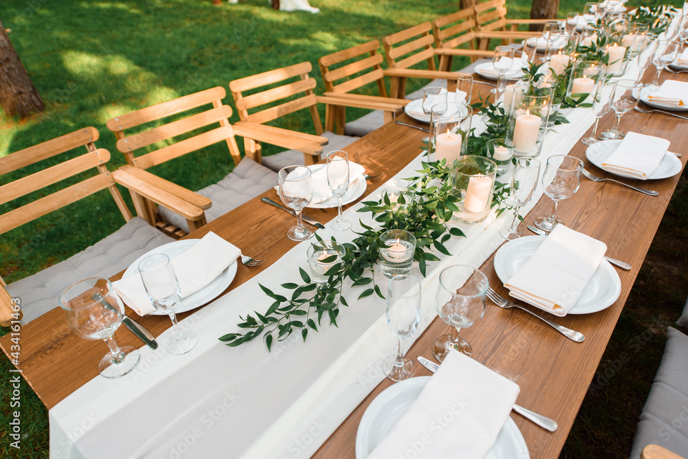 Wedding table with rustic decoration in the forest. Plates, and green branch with candles on the table. Green decoration
