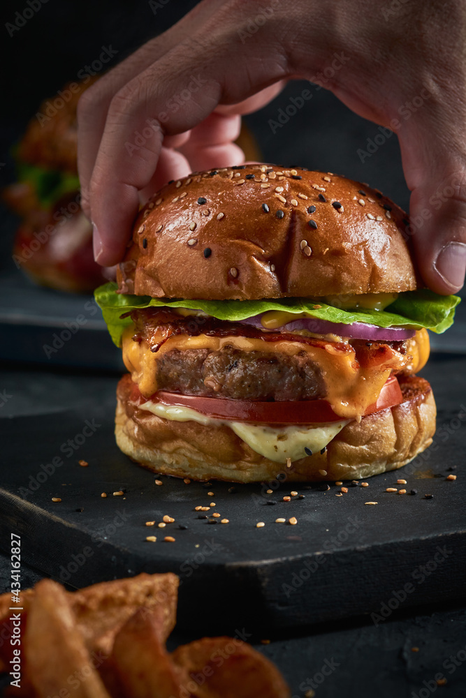 Vertical shot of a male's hand grabbing burger's upper bun Vertical shot of a male's hand grabbing burger's upper bun