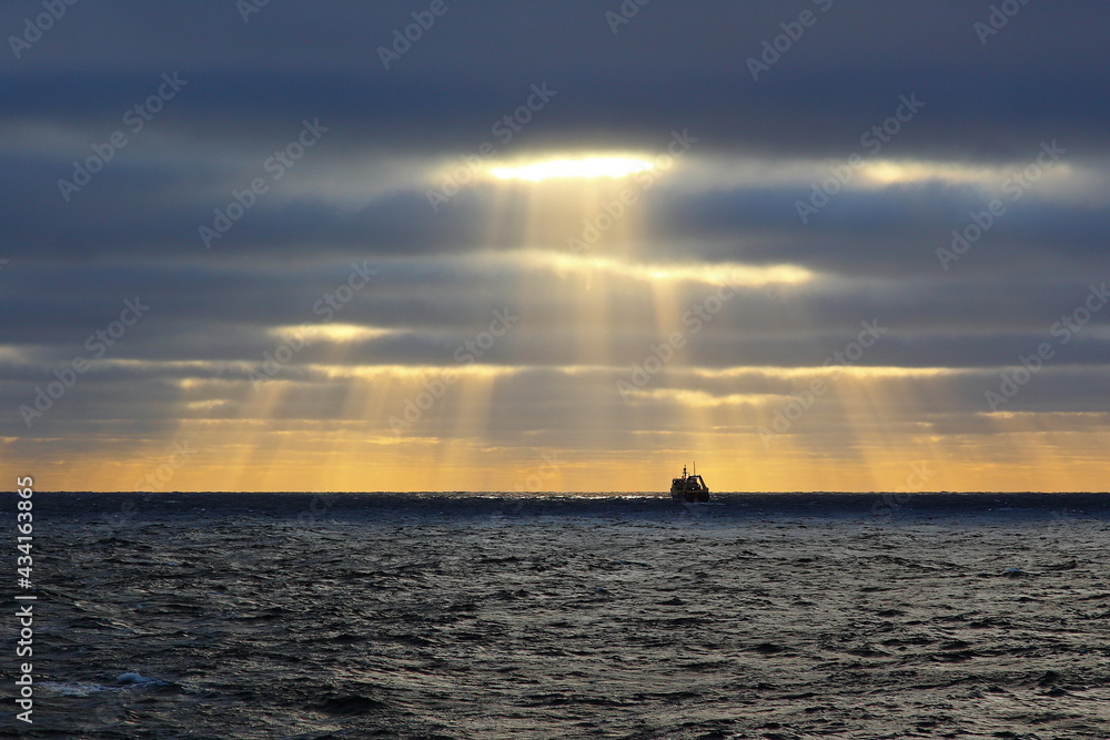 Fishing boat in the ocean against the backdrop of clouds with the sun's rays breaking through
