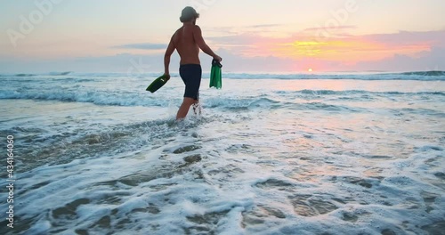 Bodysurfer walks. Young bodysurfer with fins and handplane walking into the ocean at sunrise photo