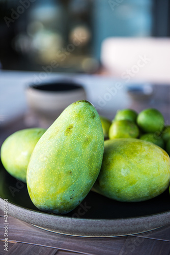 Exotic green mangoes on plate served on table with rip limes on sunny day in tropical resort photo