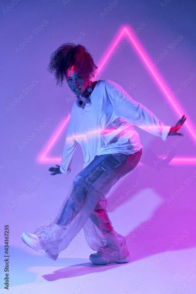 © Manuel Ruiz/ADDICTIVE STOCK - Full body talented young African American female dancer in loose clothes dancing in studio in neon lights and looking at camera