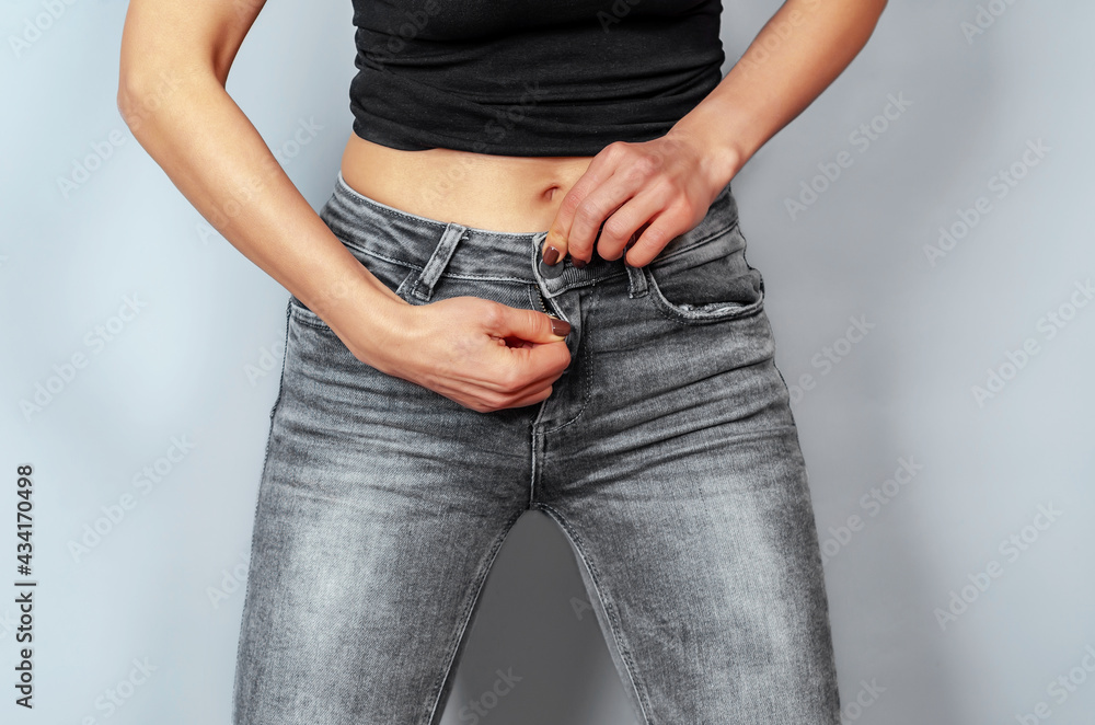 Slender woman fastens zipper in gray jeans Weight loss fitness  