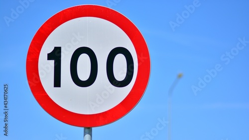 Road sign on a highway indicates a speed limit of 100 km per hour. Red circle with white center.